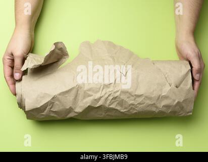 Two female hands hold rolled brown paper, green background, top view Stock Photo