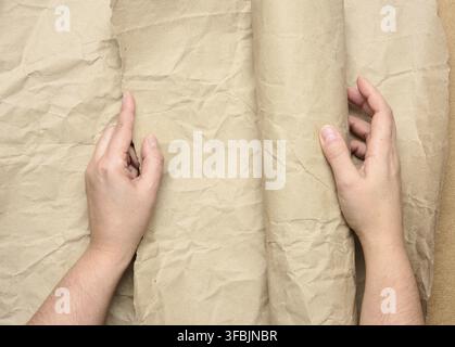 Two female hands hold rolled brown paper, top view Stock Photo