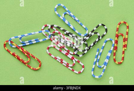 A handful of colorful striped paper clips lying haphazardly on a green paper background, close-up of school and office supplies Stock Photo