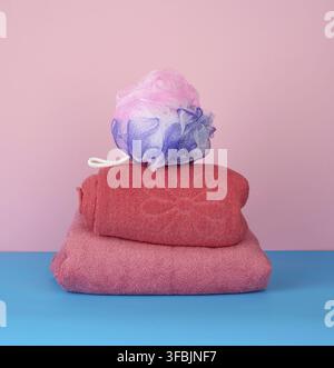 Stack of pink folded towels and a plastic washcloth on a blue background, bath set Stock Photo