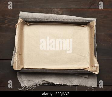Empty rectangular metal pan covered with brown parchment paper on a wooden table, top view Stock Photo