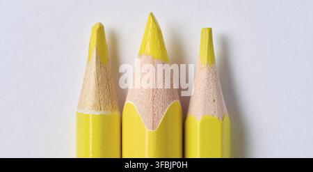 A row of yellow wooden drawing pencils with sharp tips on a white background, close up Stock Photo