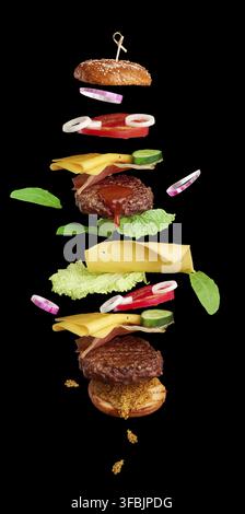 Flying burger ingredients: cutlet, sesame seed bun, tomato, onion, green lettuce, cheese on black background, delicious double cheeseburger Stock Photo