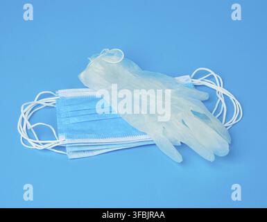 Disposable gloves and stack of medical masks made of non-woven material with white rubber bands on a blue background, protective accessory for the res Stock Photo