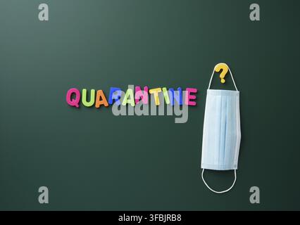 Inscription quarantine from multi-colored plastic letter on a green chalk board, hanging disposable medical mask Stock Photo
