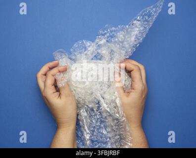 Female hand holding crumpled piece of polyethylene with air bubbles on a blue background, packing material Stock Photo