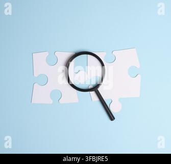 White puzzles and plastic magnifying glass on a blue background, top view Stock Photo