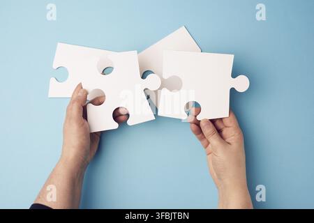 Two female hands holding big paper white blank puzzles on a blue background, concept of business Stock Photo