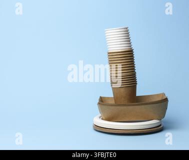 Stack of white and brown paper cups and round plates on a blue background, zero waste Stock Photo