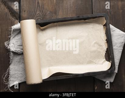 Empty rectangular metal pan covered with brown parchment paper and paper rolls on a wooden table, top view Stock Photo