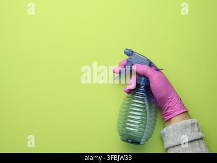 Female hand in pink glove holds a transparent plastic spray bottle on green background, copy space Stock Photo