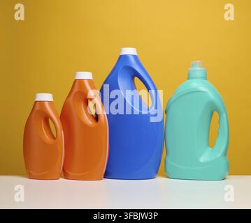 Plastic orange and blue large bottles with liquid detergent stand on a white table, yellow background Stock Photo