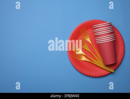 Orange plastic forks and empty red paper disposable plates on a blue background, top view, set Stock Photo
