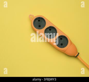 Rubber orange power strip with three sockets isolated on a yellow background, top view Stock Photo