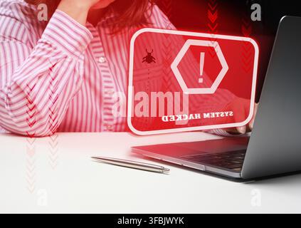 A woman sits at a laptop, in front of her is the inscription the system is hacked. User hacker attack, system hacking, password stolen Stock Photo