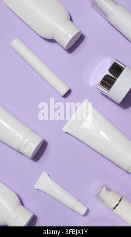 A variety of white plastic tubes and bottles with cosmetics arranged randomly on a lavender background. Top view Stock Photo