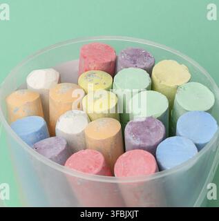Multicolored chalk in a plastic bucket on a green background, close up Stock Photo