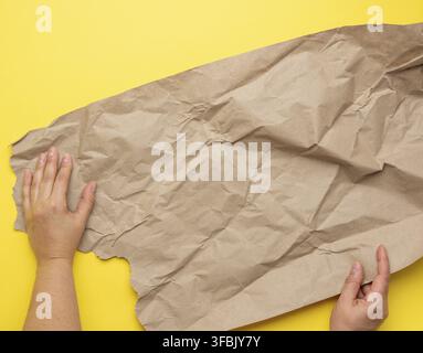 Two hand holds piece of crumpled brown paper on a yellow background, element for designer, top view Stock Photo