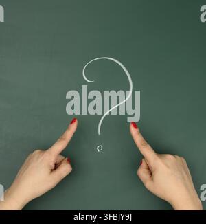 A question mark drawn in white chalk and female hands point a finger at it. Question and answer concept, search for truth, uncertainty Stock Photo