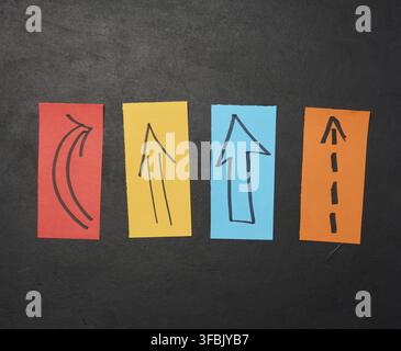 Drawn various arrows on paper scraps against a black background, symbolizing the concept of diversity, direction, and contrast Stock Photo
