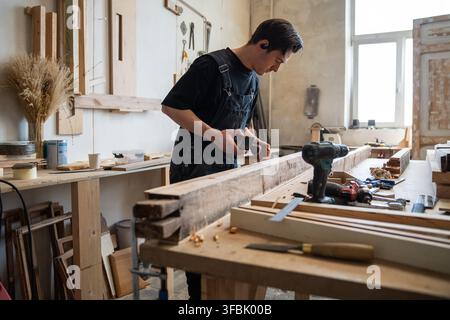 Professional craftsperson restoring window frame in workshop, using hand plane tool at workbench. Stock Photo