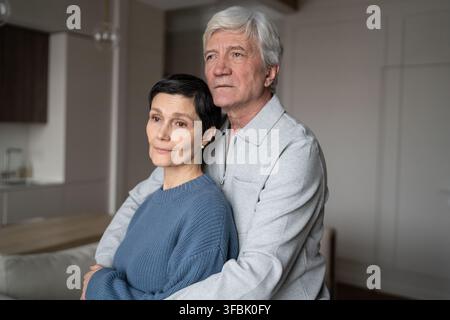 Thoughtful senior man hugging wife with love. Elderly couple hug, marital care, calm aging together Stock Photo