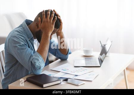 Stressed Black Entrepreneur Sitting At Desk And Looking At Financial Papers Stock Photo