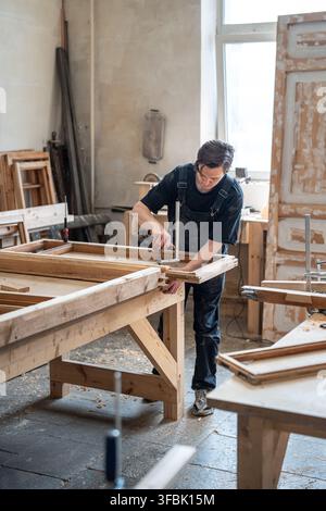 Professional carpenter secures parts of antique wooden window frame to workbench using clamps tools. Stock Photo