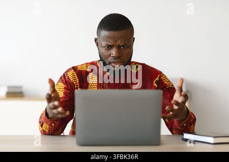 Computer Problems. Frustrated African Businessman In Traditional Clothes Having Troubles With Computer Stock Photo