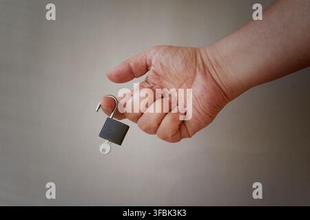 A person's hand holds a small padlock with a key. Stock Photo