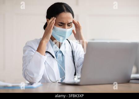 Female doctor in protective face mask having headache Stock Photo