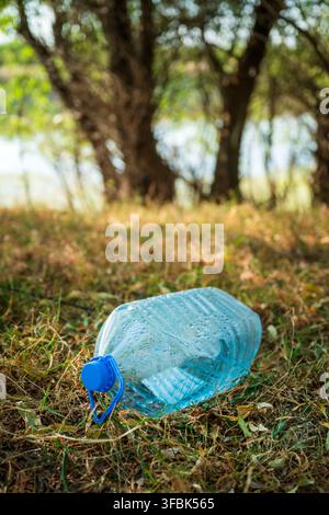 Discarded plastic jug lying on dry riverbank grass. Concept of environmental plastic pollution, eco-system contamination, waste management issues, and Stock Photo