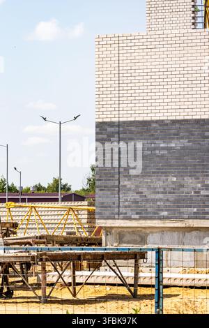 Vertical shot of a multi story residential building wall built with white and grey bricks next to scaffolding equipment Stock Photo