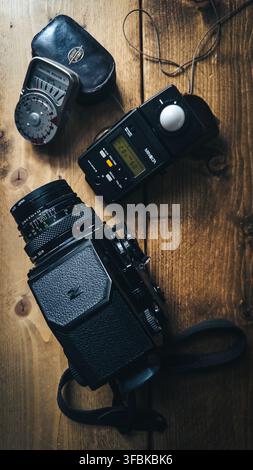 Bronica ETRS medium format film camera with interchangeable lens, light meter, leather case and camera strap arranged on a rustic wooden table, illust Stock Photo