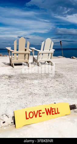 Sea view from the shoreline at GoldenEye resort, Jamaica, with two white Adirondack chairs facing the Caribbean Sea and a yellow hand-painted sign rea Stock Photo