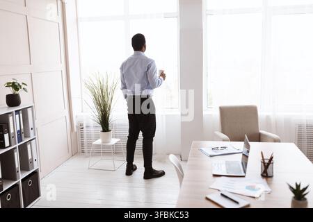 African american businessman drinking coffee near window, back view Stock Photo
