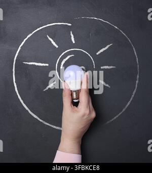 A human hand holding a light bulb, a chalk outline of the bulb with rays. Concept of a new idea Stock Photo