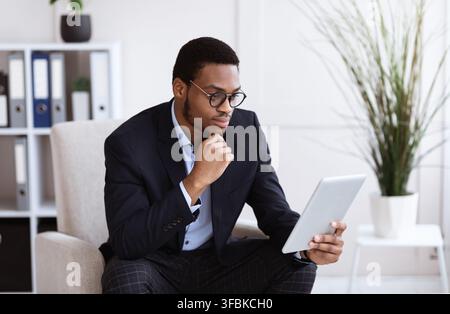 Concentrated black entrepreneur in glasses using digital tablet Stock Photo
