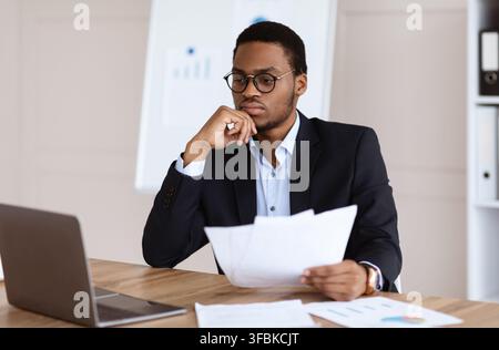 Worried black manager holding marketing report, using laptop Stock Photo