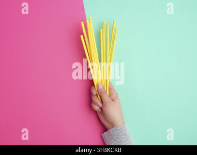 Hand holds a stack of yellow paper tubes for a cocktail on a multi-colored background, concept of rejection of plastic and the use of recyclable mater Stock Photo