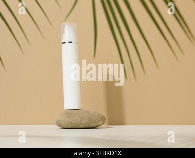 White plastic cosmetic bottle with dispenser and transparent cap on brown background. Packaging for cream, fluid and gel Stock Photo