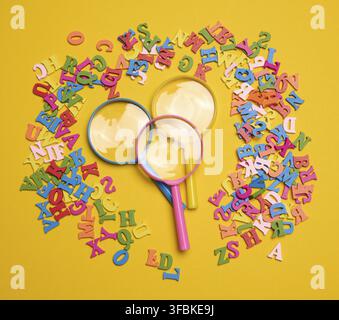 Plastic magnifying glass and wooden letters of the English alphabet on a yellow background, top view Stock Photo