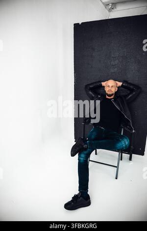 A man relaxes on a chair with arms resting behind his head in a studio setting. Stock Photo