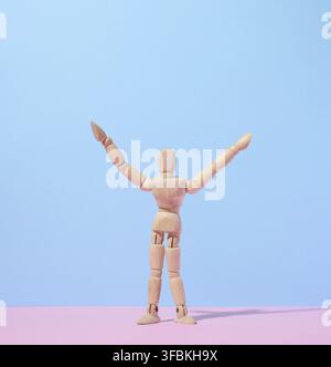 Wooden puppet man on a blue background, arms raised up Stock Photo