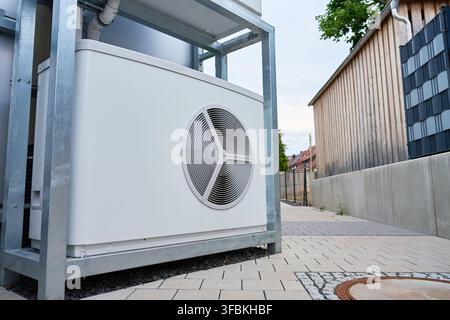 Outdoor heat pump unit installed beside a residential building. Close-up of home heating and cooling equipment with a large fan mounted on a metal sup Stock Photo