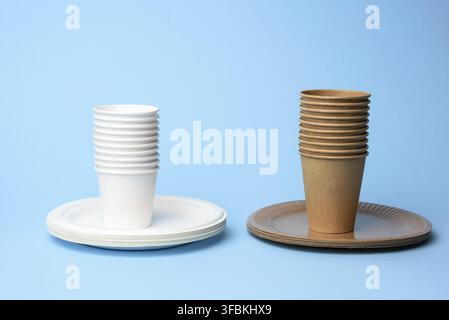 Stack of white and brown paper cups and round plates on a blue background, zero waste Stock Photo