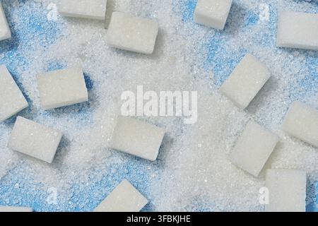 White cubes of refined sugar and scattered crystal sugar on a blue background Stock Photo