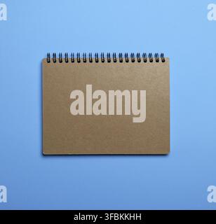 Notebook on a black iron spring with brown empty sheets on a blue background, close up Stock Photo