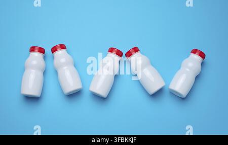 White plastic bottles with red caps for dairy products on a blue background, top view Stock Photo