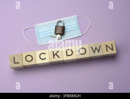 Disposable medical mask and and wooden blocks with the inscription lockdown on a purple background. Self-isolation concept to prevent the spread of vi Stock Photo